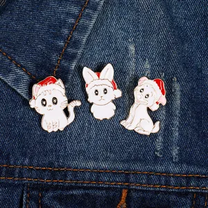 Three enamel Christmas pins with cats and dogs in red hats on blue denim fabric