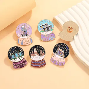 Whimsical crystal ball enamel pins featuring magical castle landscapes and Let it snow text
