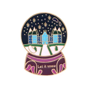 Macro shot of an enamel crystal ball brooch with castle design and Let It Snow text