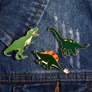 Drei grüne Dinosaurier-Emaille-Pins an einem Jeansjackenaufschlag mit feiner Goldumrandung