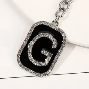 Primer plano del llavero letra G en metal plateado con pedrería brillante y esmalte negro
