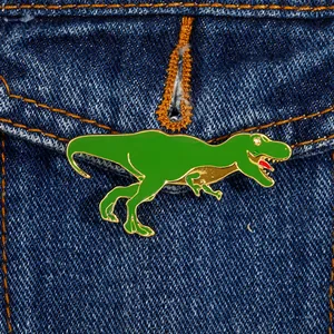 Makroaufnahme einer grünen T-Rex Emaille-Brosche an einer dunkelblauen Jeansjackentasche