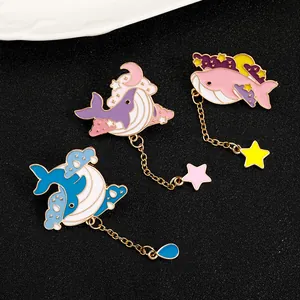 Detailed view of enamel whale brooches in blue, pink, and purple with hanging charms