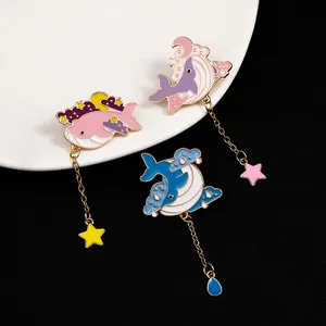 Detail of whale enamel pins with star pendants and gold chains on a white tray