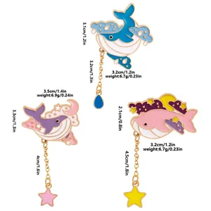 Set of three whale enamel pins with clouds, stars, and moon pendants on white background
