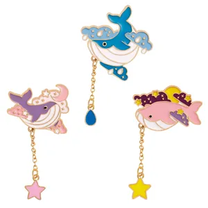 Three colorful whale enamel pins with gold chains, stars and cloud charms on white background