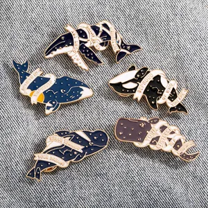 Detail of five enamel ocean pins on denim featuring whales and motivational quotes