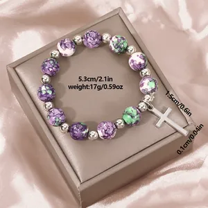Detail view of natural stone beaded bracelet with silver cross on a silk background