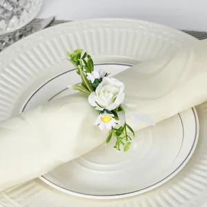 Eleganter Serviettenring mit weißer Rose, Gänseblümchen und Beeren auf einem weißen Teller