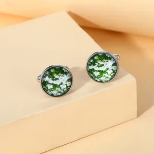 Close-up of round silver cufflinks featuring white daisy pattern and green floral glass inlay