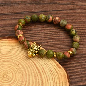 Close-up of natural unakite stone beads and golden wolf head charm on a wooden background