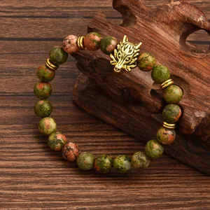 Macro detail of natural unakite beads with a gold wolf head charm on a wooden stand