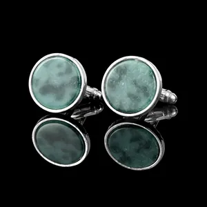 Close-up of vintage silver cufflinks with round green marble stones on a black reflective surface