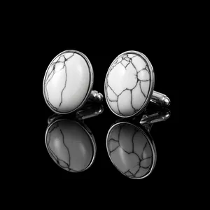 Macro detail of silver cufflinks with oval white marble stone inlay on a black background