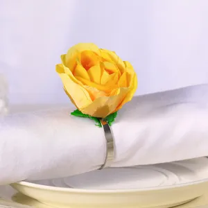 Detalle de servilletero con rosa amarilla artificial y aro de metal sobre tela blanca