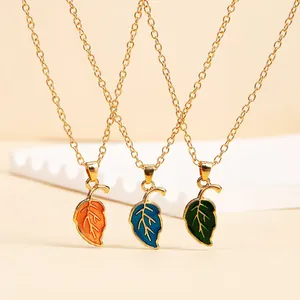 Detailed macro view of three gold leaf necklaces featuring orange, blue, and green enamel finishes
