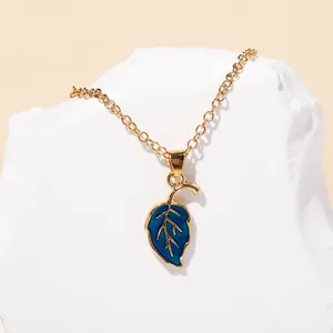 Detailed macro view of a gold leaf pendant necklace with blue enamel on a white stone base