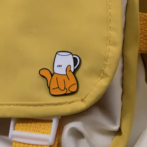 Détail d'un pin's émaillé de chat orange mignon dans une tasse blanche sur un sac