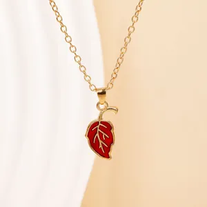 Minimalist gold chain necklace with a red leaf enamel pendant on a warm beige background