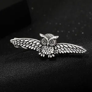 Detailed view of silver owl necktie clip with intricate wing textures on black surface
