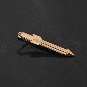 Macro shot of gold arrow-shaped tie clip with polished finish on black leather texture