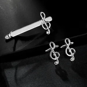 Polished silver musical note tie clip and cufflinks set on textured black background