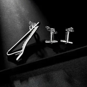 Close-up of silver-tone musical note tie clip and cufflinks set on black background