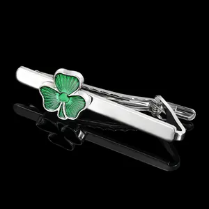 Polished silver tie clip with vibrant green clover leaf detail on a black background