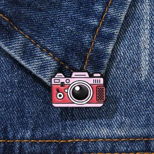 Retro camera enamel brooch in pink and red pinned on blue denim fabric background