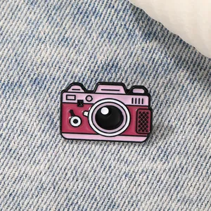 Macro detail of a vintage pink enamel camera pin displayed on blue denim fabric