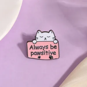 Detail van cartoon kat emaille speld met tekst Always be pawsitive op roze bord