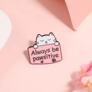 Detail van witte cartoon kat emaille speld met Always be pawsitive tekst op roze