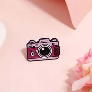 Macro shot of vintage pink camera enamel pin on soft silk floral background