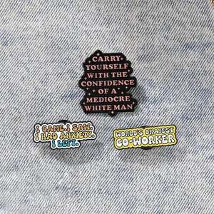 Macro shot of three creative enamel phrase brooches on denim for bag and lapel decor