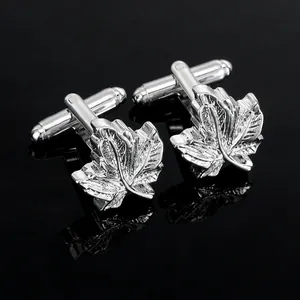 Close-up of polished silver maple leaf cufflinks with detailed vein texture on black surface