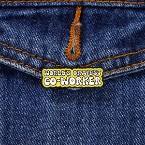 Detail of 'WORLD'S OKAYEST CO-WORKER' enamel pin badge on blue denim jacket pocket