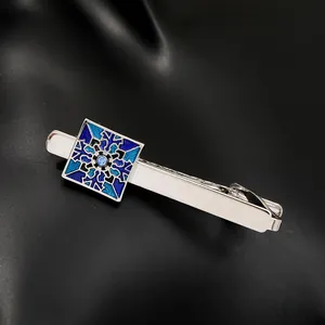 Macro detail of men's silver tie clip with blue enamel patterns and center crystal stone
