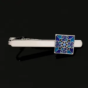 Close-up of silver tie clip with blue geometric pattern and crystal on black mirror