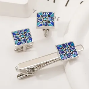 Close-up of silver tie clip and cufflinks set with blue geometric enamel patterns