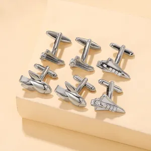 Macro view of silver rocket and space shuttle cufflinks on a textured beige surface