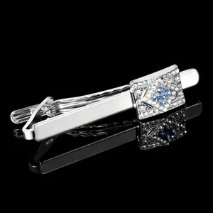 Macro detail of silver square necktie clip with blue floral stones on black reflective surface
