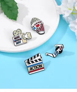 Detail of movie theme enamel pins showing popcorn, camera and clapboard on a white plate