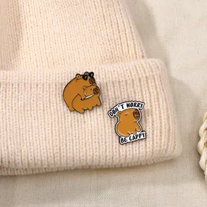 Close-up of cute enamel capybara badges on a beige knitted hat with Cappy slogan
