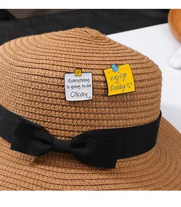 Détail de broches en émail avec citations inspirantes sur un chapeau de paille