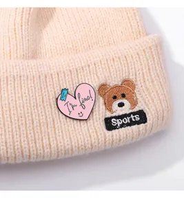 Détail d'un bonnet en tricot avec écusson cœur rose et broderie d'ours