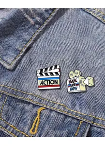 Close-up of cinema clapperboard and vintage camera enamel pins on denim jacket