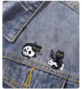 Detail of cartoon black cat enamel pins with skull and weapon designs on denim jacket