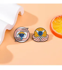 Detail of creative enamel blue eye brooches with wings and surreal hand motifs on orange base