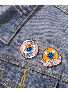 Close-up of enamel eye pins with wings and teardrop designs on blue denim jacket