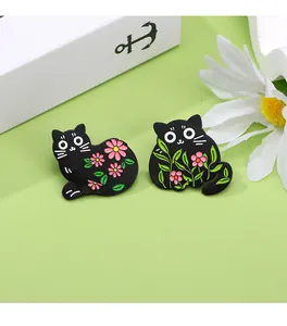 Close-up of black cat enamel pins with floral patterns on a soft green background